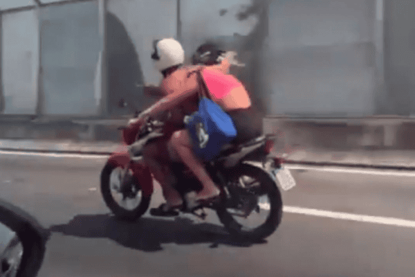Mulher na garupa pilota moto enquanto namorado aproveita trajeto para comer marmita