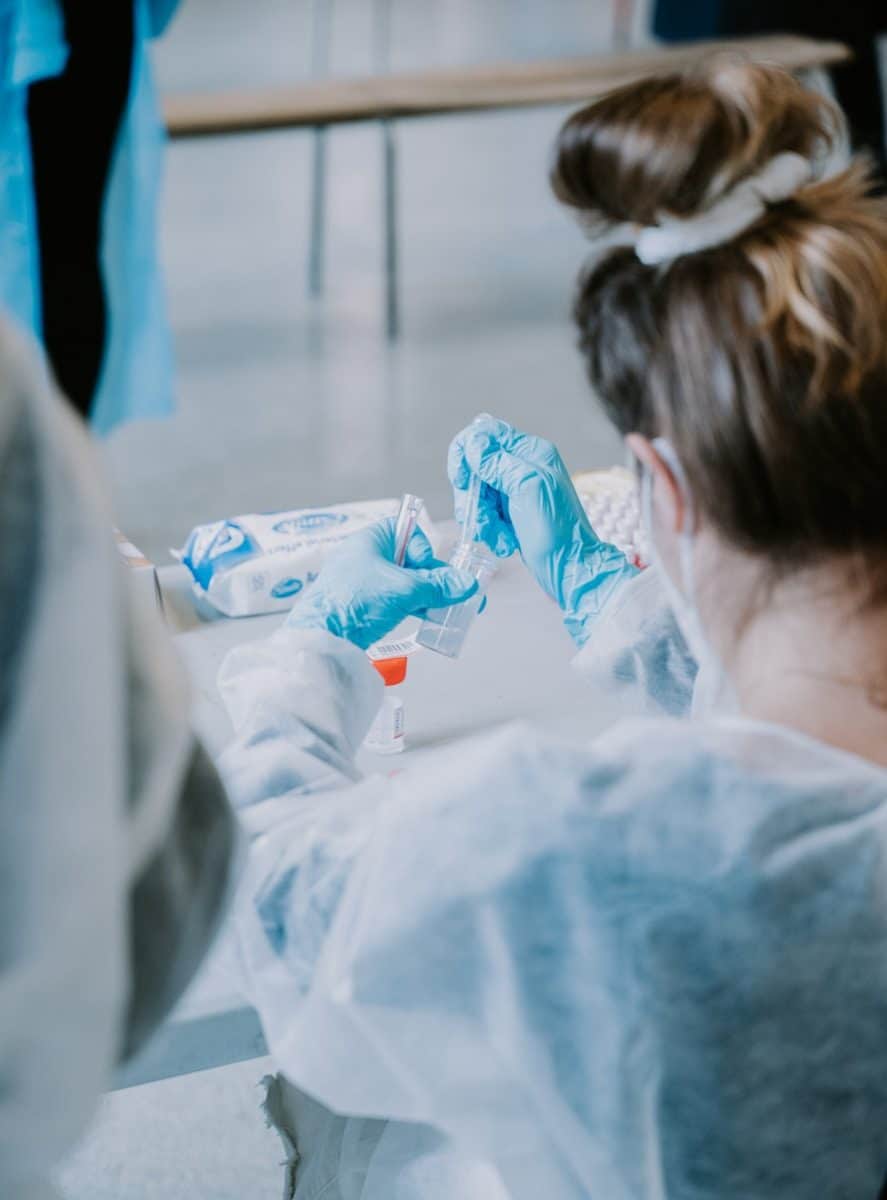 A person in blue gloves handling small vials at a table