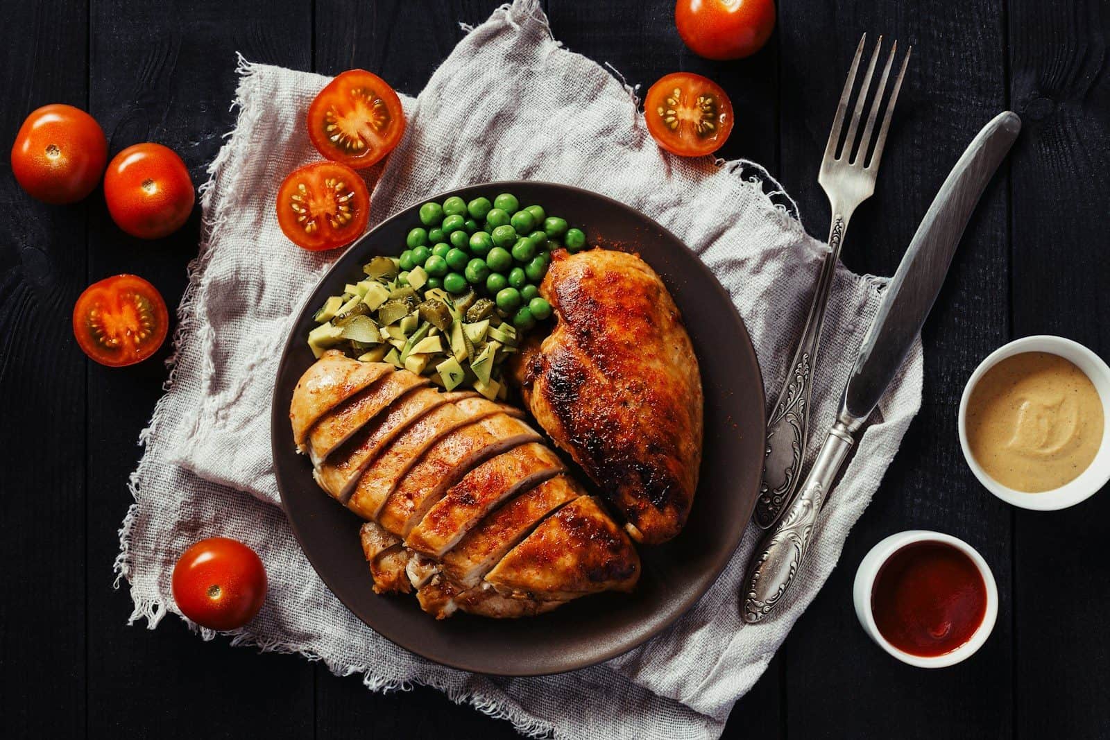 Sliced chicken breast with green peas and chopped pickles on a dark plate