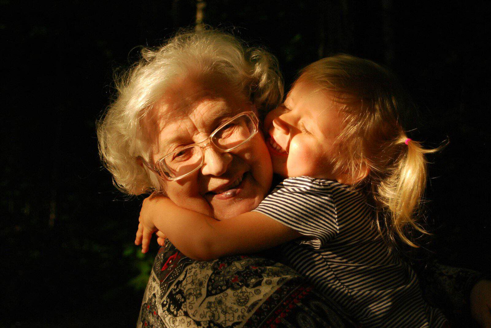 An elderly woman with white hair and glasses hugging a young child