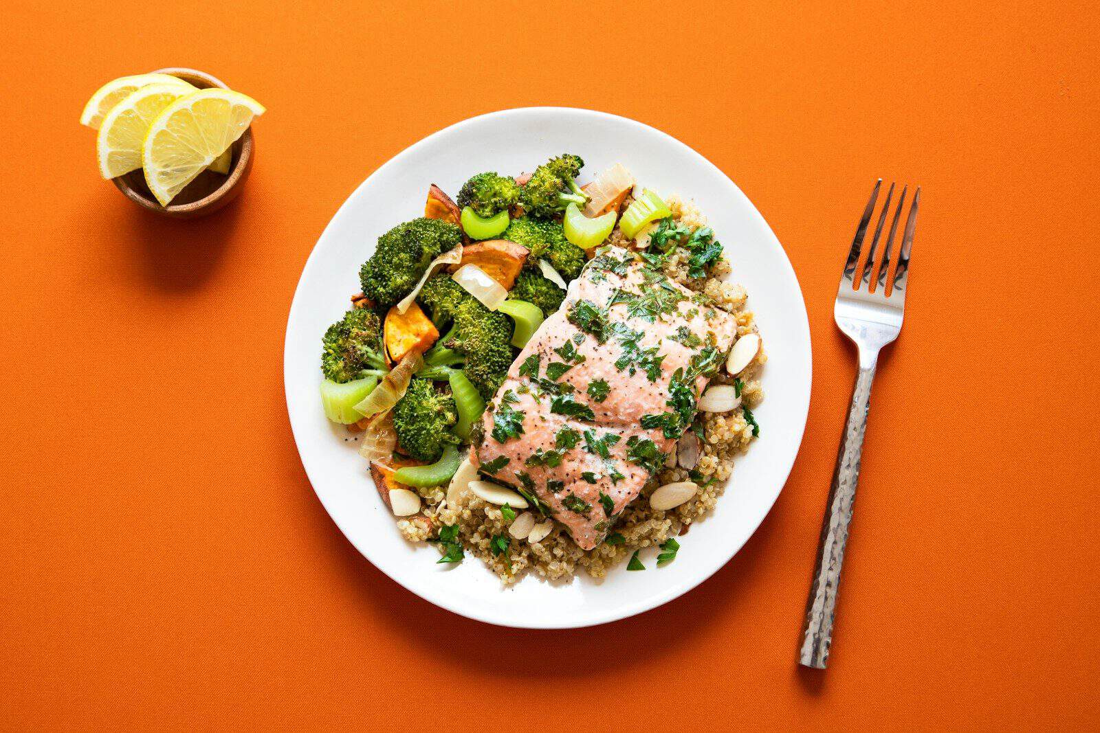 A salmon fillet with herbs on quinoa beside roasted broccoli and celery on a plate