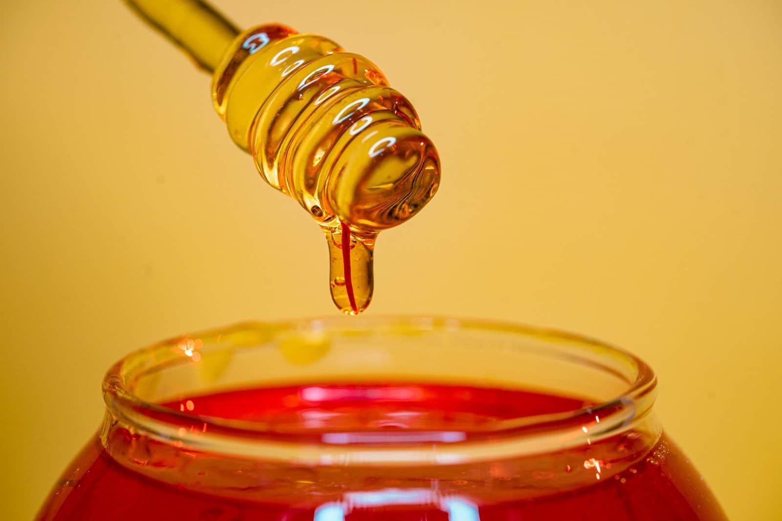 Golden honey dripping from a wooden dipper into a glass jar