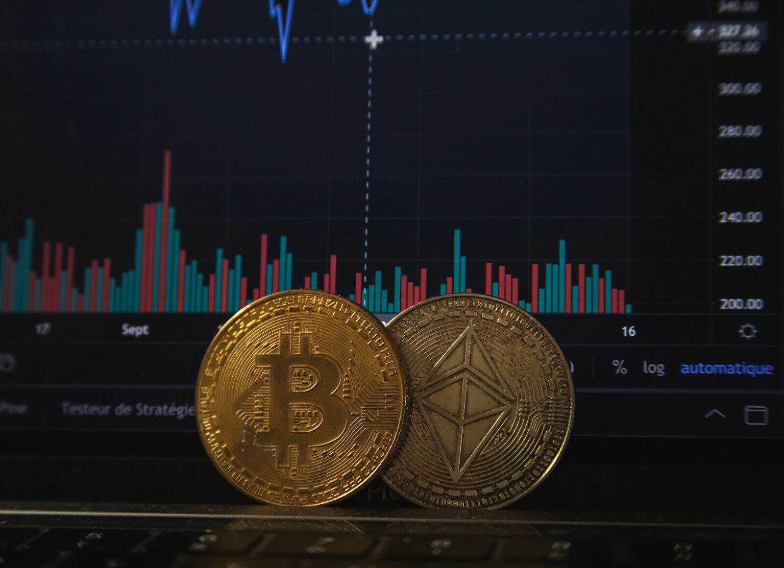 Gold Bitcoin and silver Ethereum coins resting on a laptop keyboard before a trading chart
