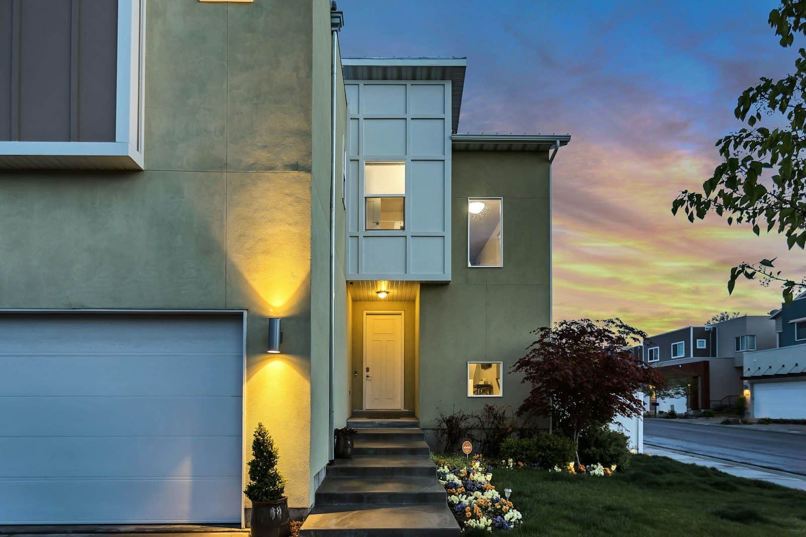 A modern house with a garage and lit doorway under a colorful evening sky