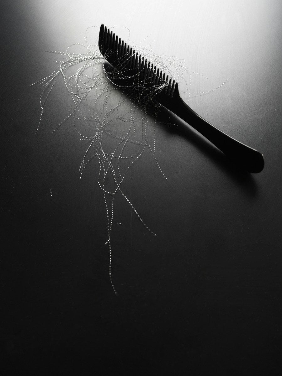 Black comb with strands of hair on dark surface