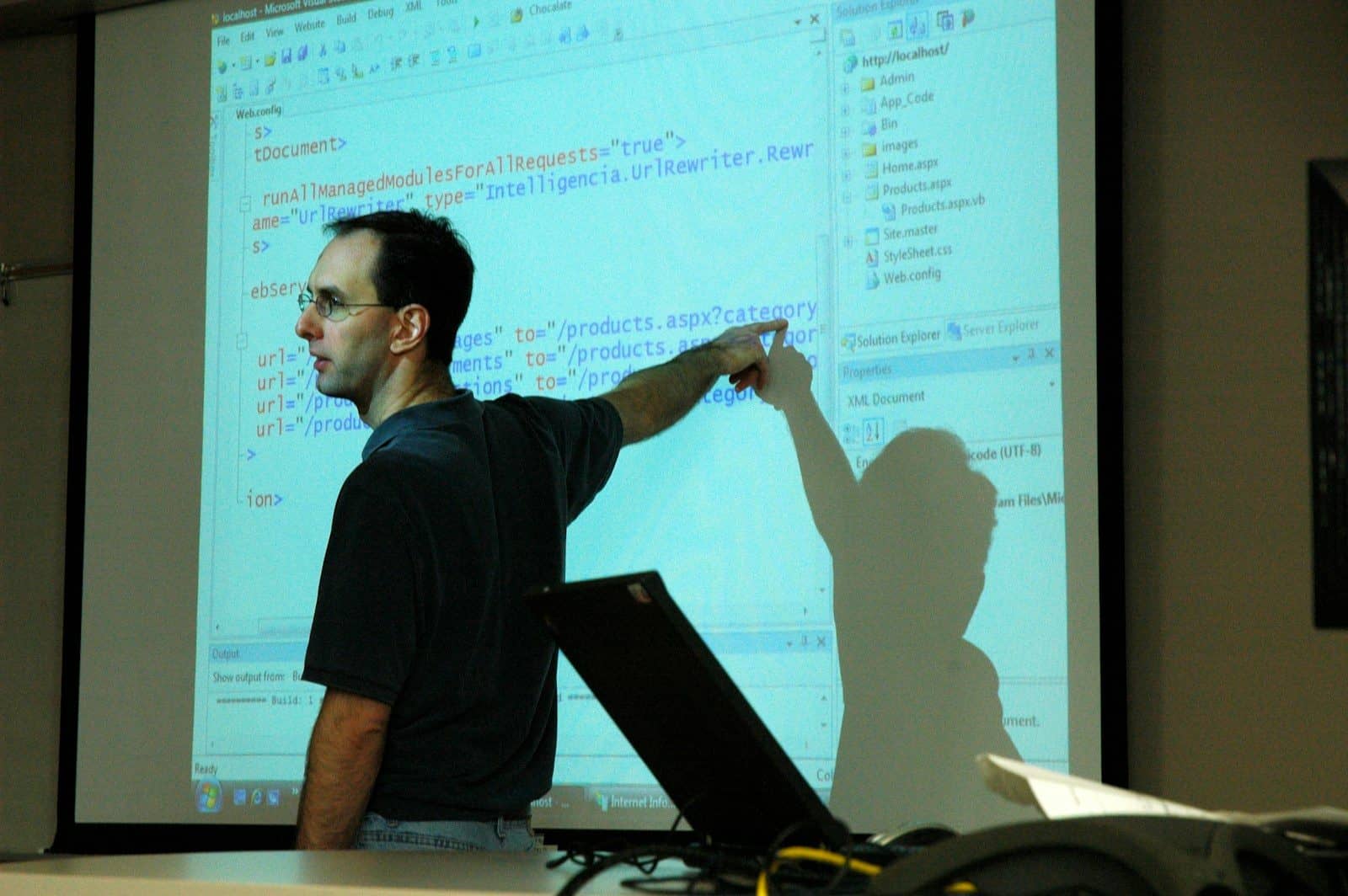 A man pointing at computer code projected on a screen in a workspace