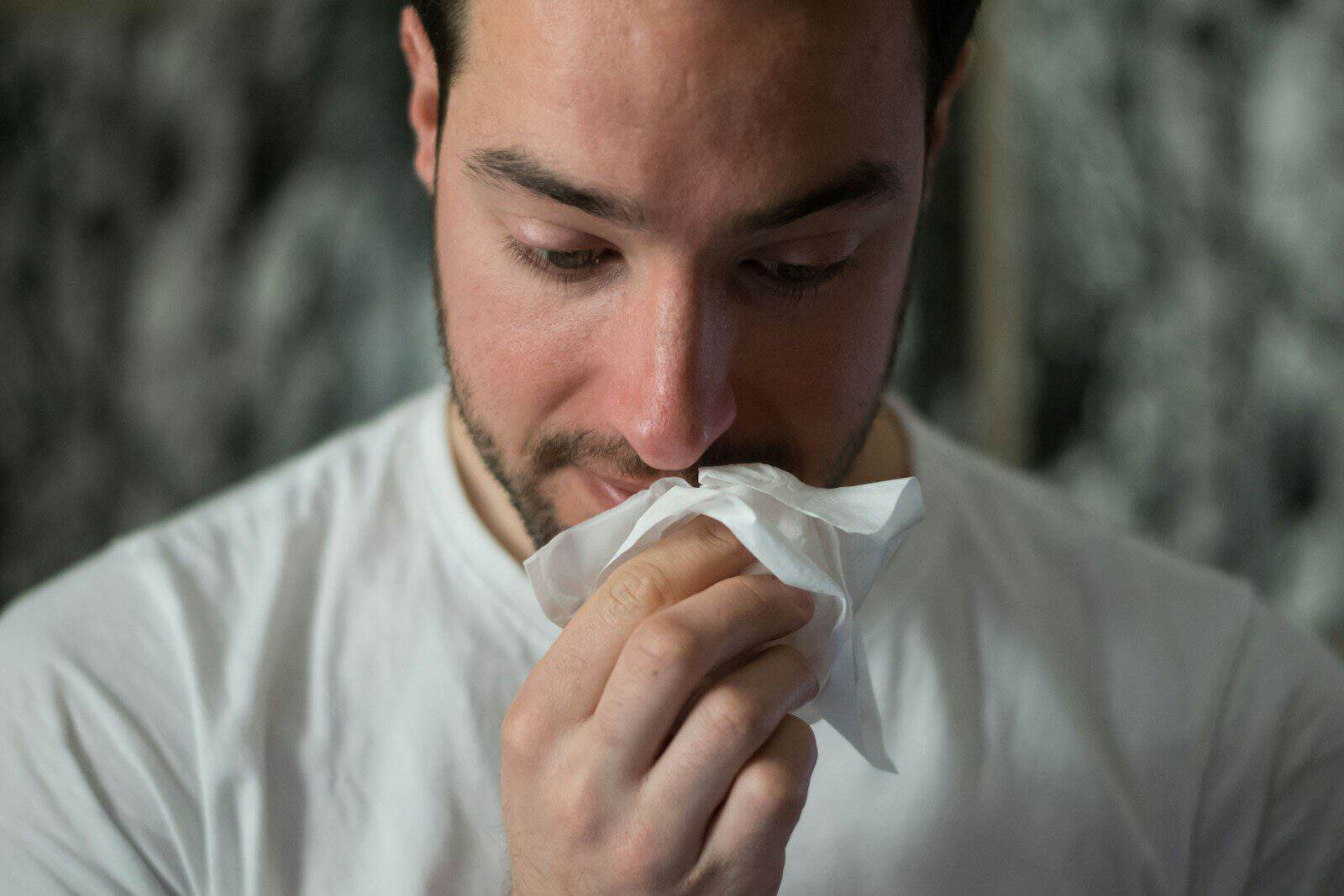 sick man blowing nose into tissue