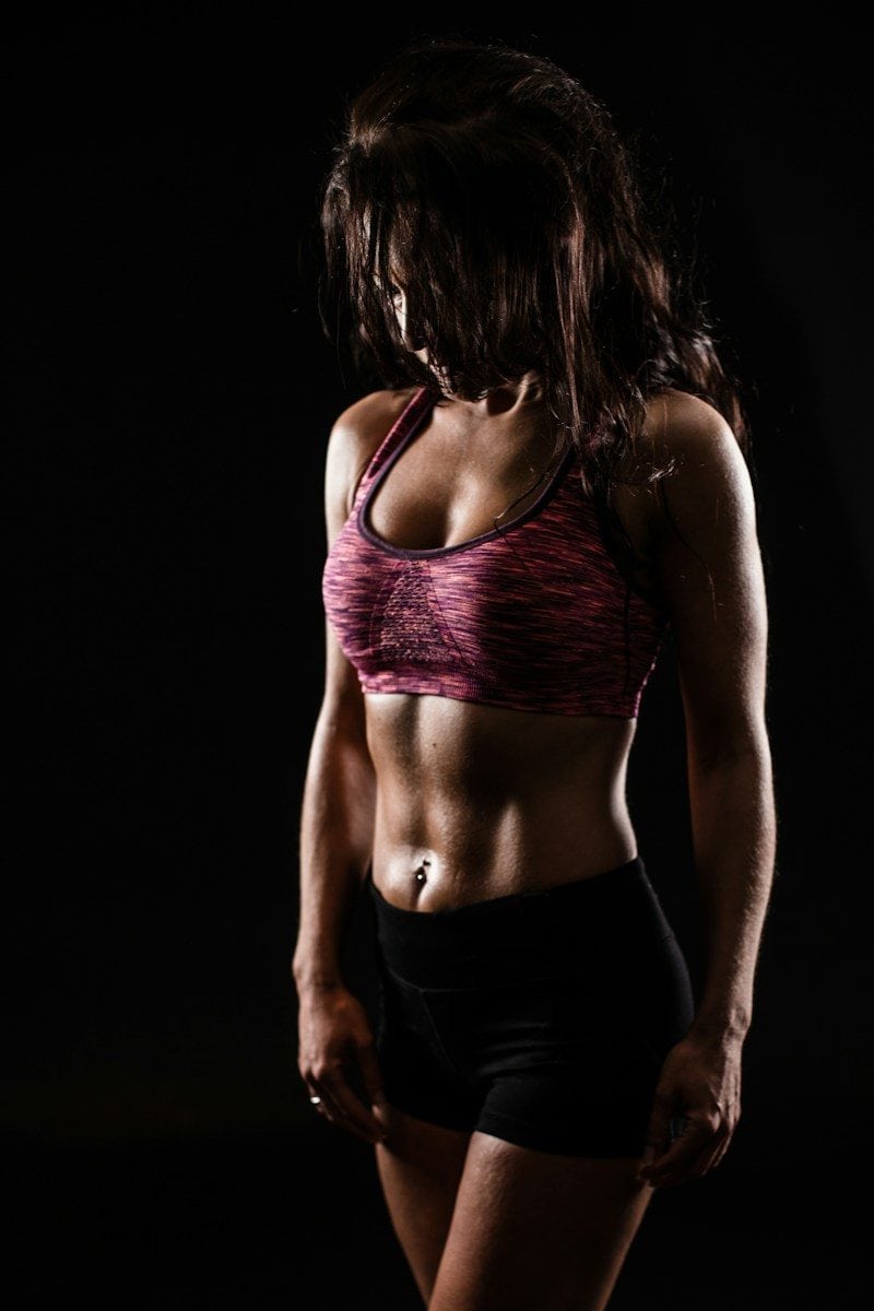 Fit woman in sports bra and shorts on black background