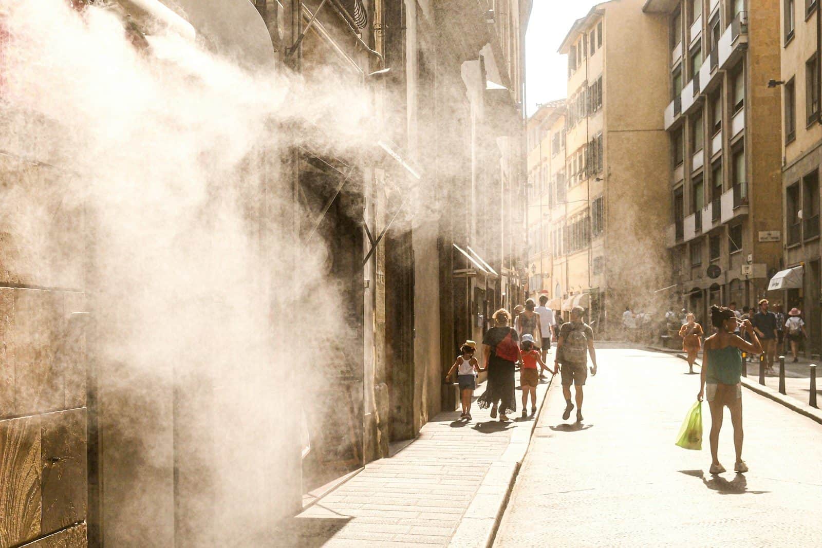 People walk down a sunny street with misting spray