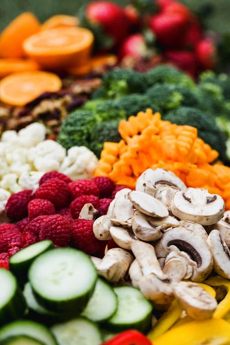 Fresh broccoli, cauliflower, raspberries, sliced mushrooms, and cucumbers arranged for a healthy meal