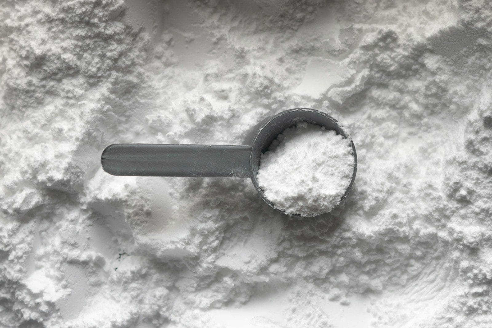 A grey plastic scoop filled with white powder resting on a pile of powder