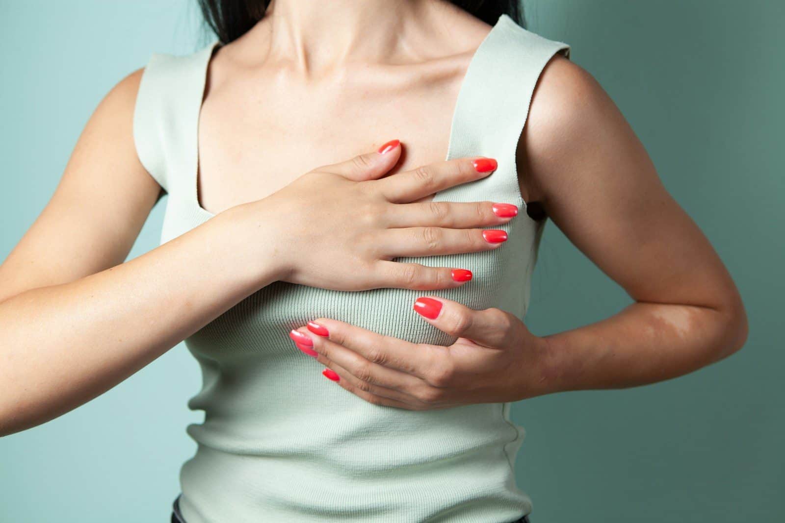 Woman performing breast self-examination against a teal background