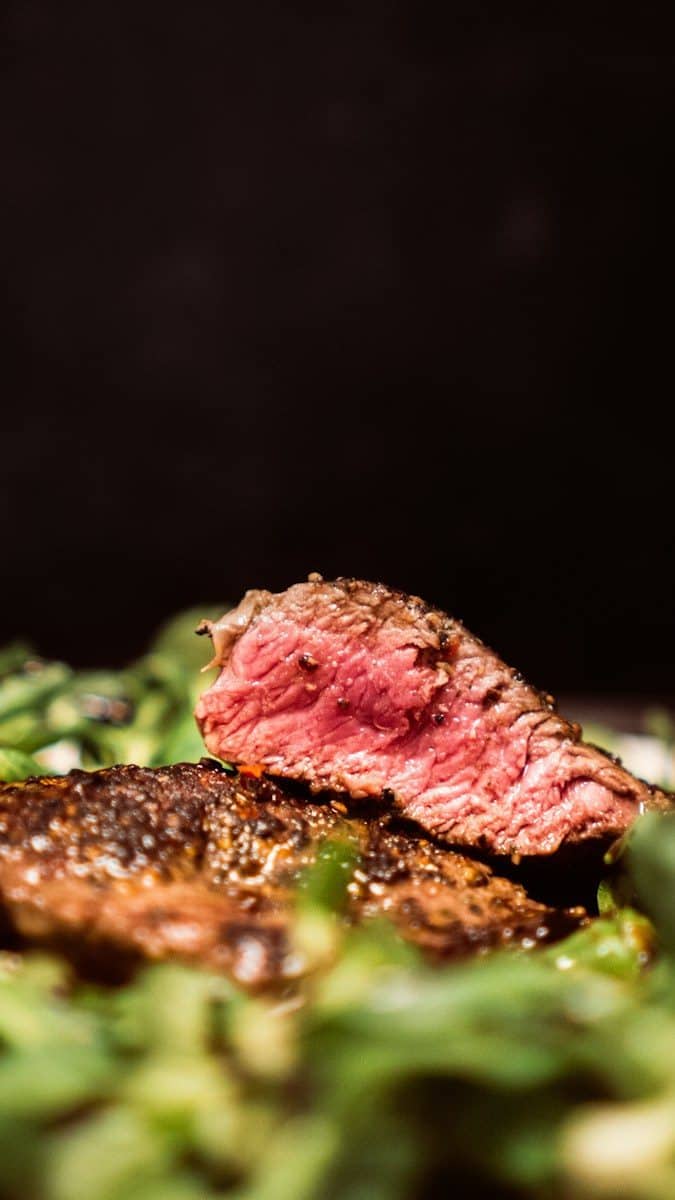 A seared steak with a pink center resting on fresh green salad leaves