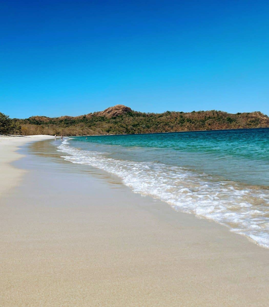 A tropical beach with calm blue water and green hills