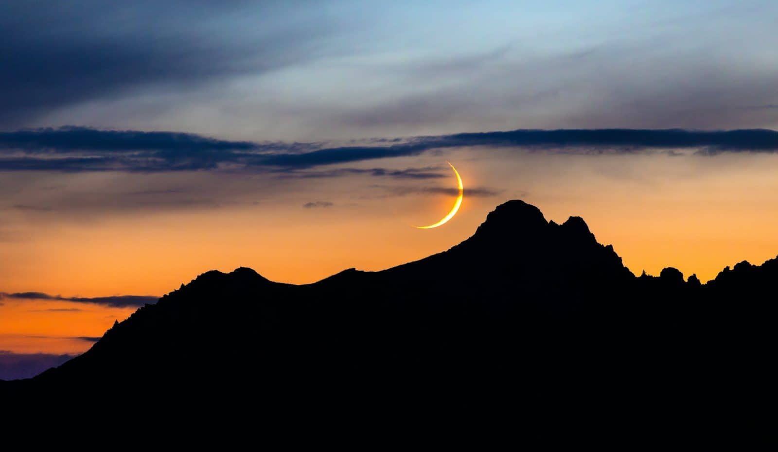 Crescent moon over silhouetted mountains at sunset