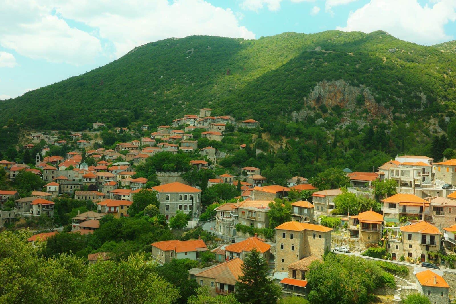 A village with orange-tiled roofs nestled on a green mountain slope in Greece