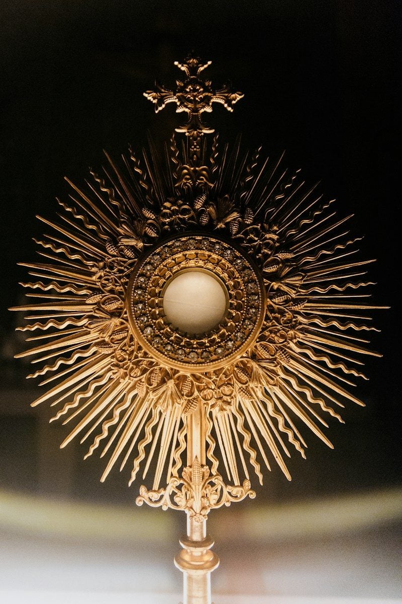 A golden monstrance with a central host and radiating sunburst rays