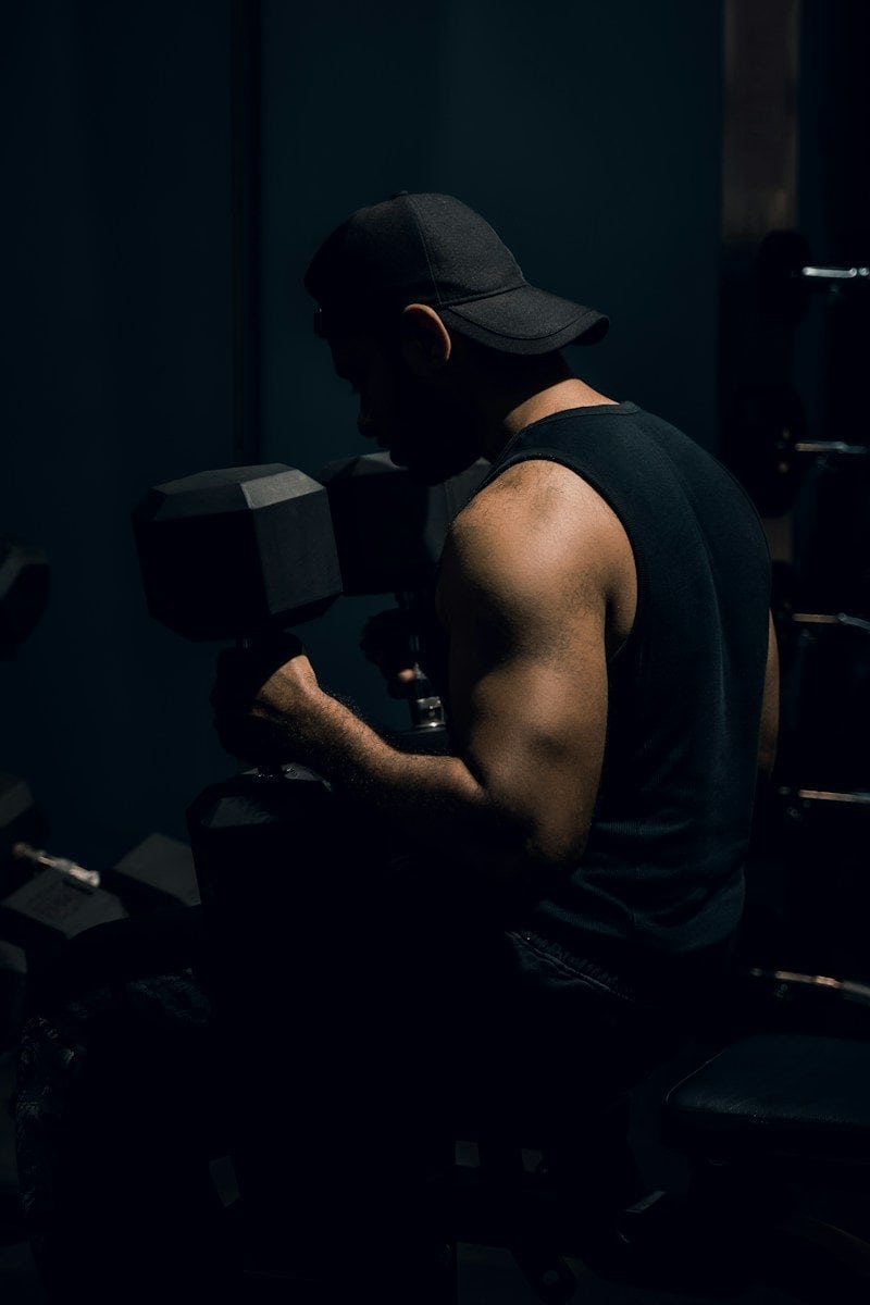 A person in a black tank top and cap lifting a dumbbell in a gym