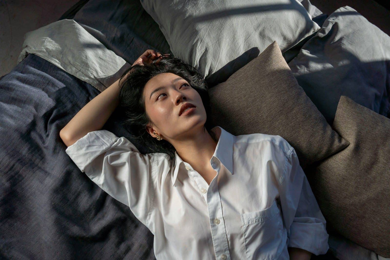 A woman in a white shirt lies on a bed