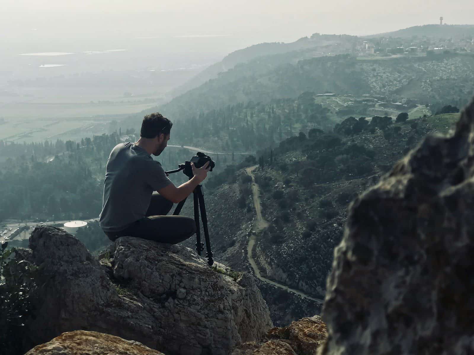 man sitting on rock using camera