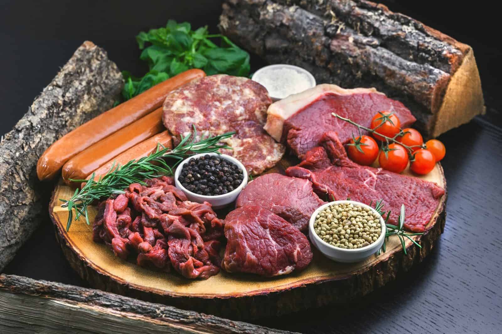 Assorted raw meats, sausages, and spices on a wooden board with rosemary
